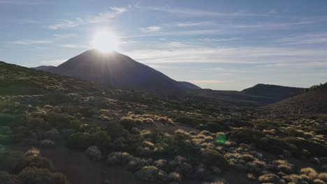 tres excursionistas parados en la ladera debajo de la montaña pico de teide en las islas canarias y viendo la puesta de sol detrás de su cumbre entre rocas y arbustos