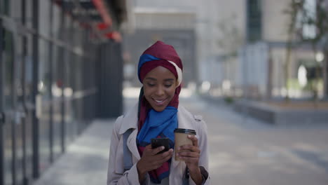 Retrato-De-Una-Joven-Mujer-De-Negocios-Afroamericana-Que-Usa-Un-Teléfono-Inteligente-Y-Disfruta-Relajándose-En-El-Almuerzo-Enviando-Mensajes-De-Texto,-Navegando-Por-Mensajes-Leyendo-Correos-Electrónicos-Usando-Un-Velo-Hijab-En-La-Ciudad