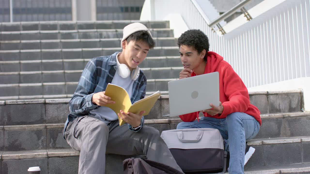 Estudiantes asiáticos y afroamericanos comparando papeles y carpetas en los escalones de la escuela