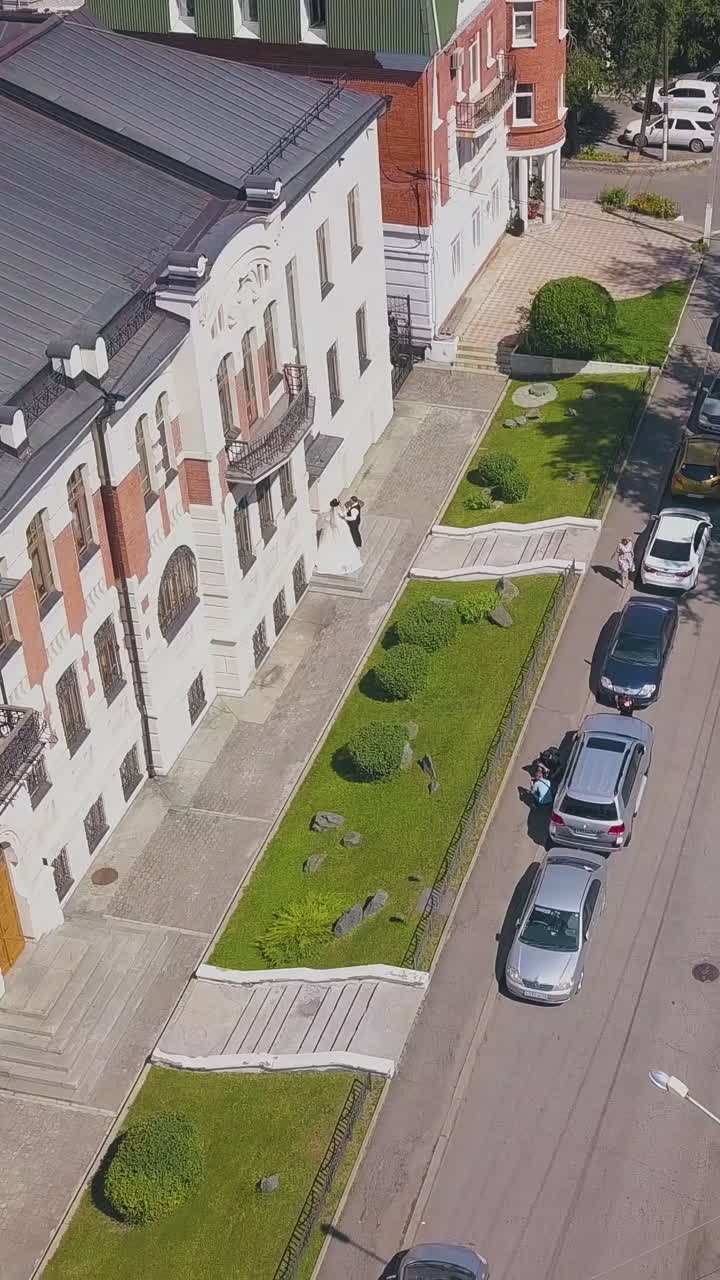 newly wedded couple walks along beautiful building in street with cars on sunny day bird eye view
