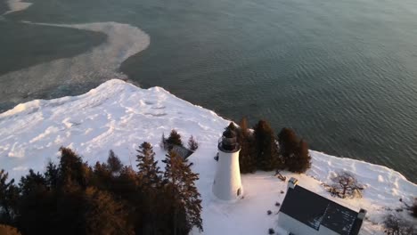 old presque isle lighthouse in michigan during the winter with a sunset