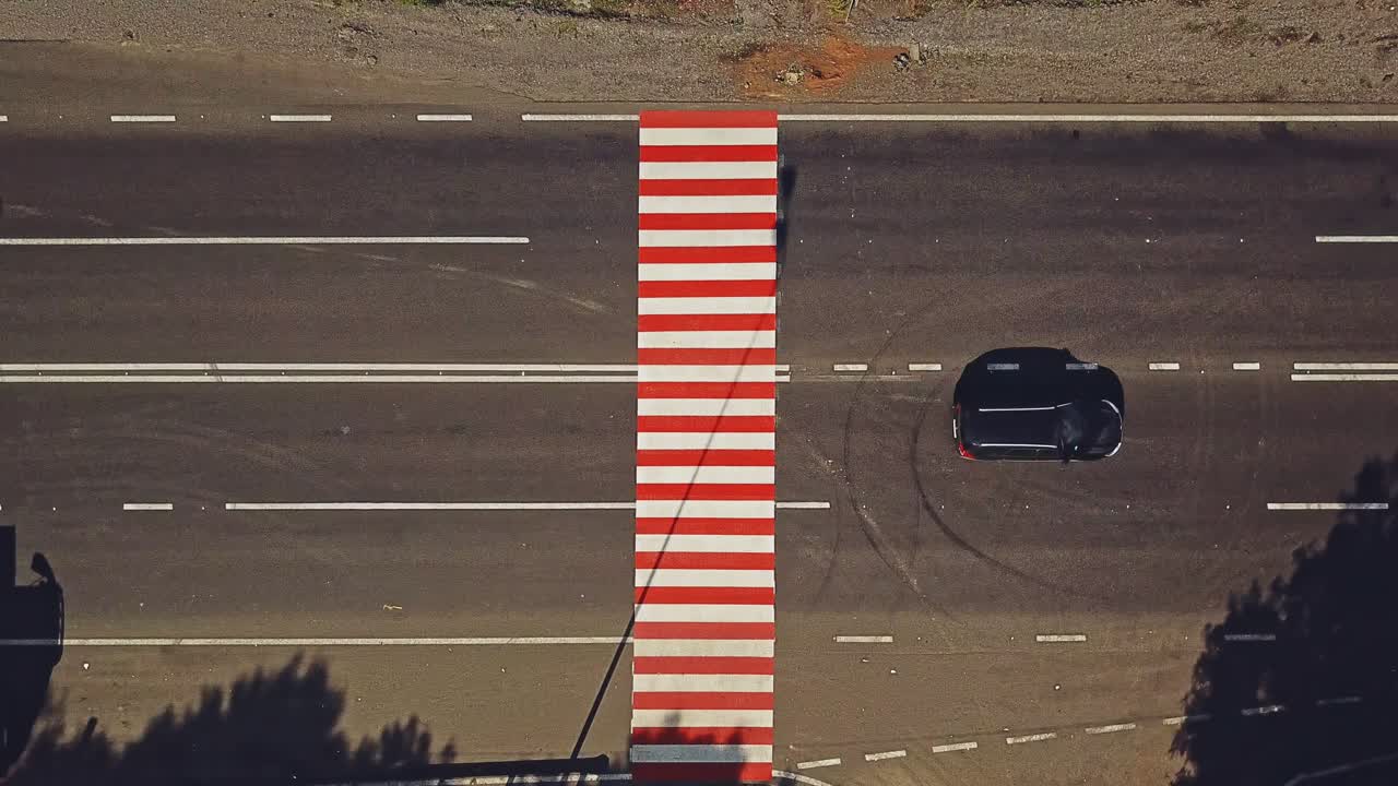 White truck and some cars passing the pedestrian crossing painted with red and white stripes on the road. Zebra crossing on asphalt and cars. Aerial view