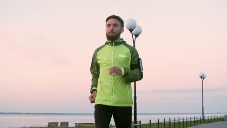 tilt down of young man in sports clothes running along riverside promenade in the city at sunrise