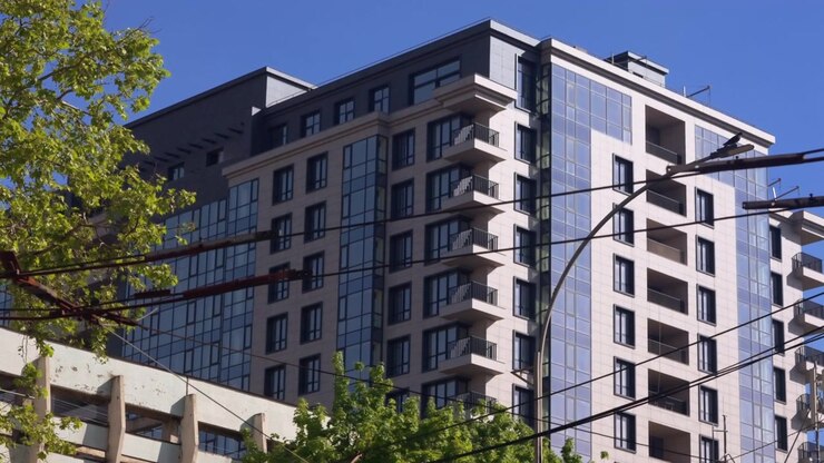 Edificio residenziale contemporaneo con facciate in vetro e balconi, sullo sfondo di un cielo azzurro e limpido.