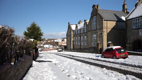 man walking down snowy hill near old school building, wide, static