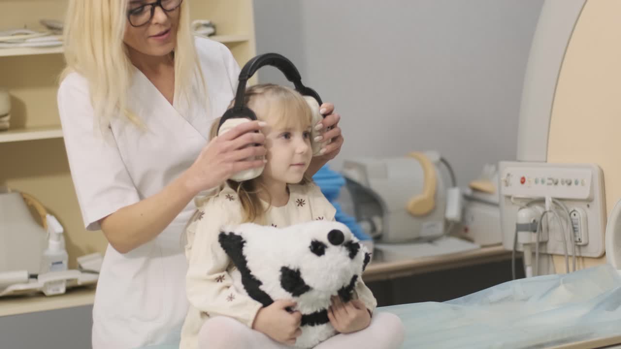 방사선 전문의는 환자에게 소음을 격리하는 헤드폰을 착용합니다.mri 스캐닝 검사를 하기 위해 어린 소녀는 자동 테이블에 앉아 있습니다.