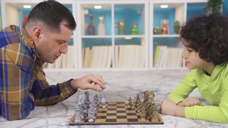 father and son lying on the floor playing chess at home.