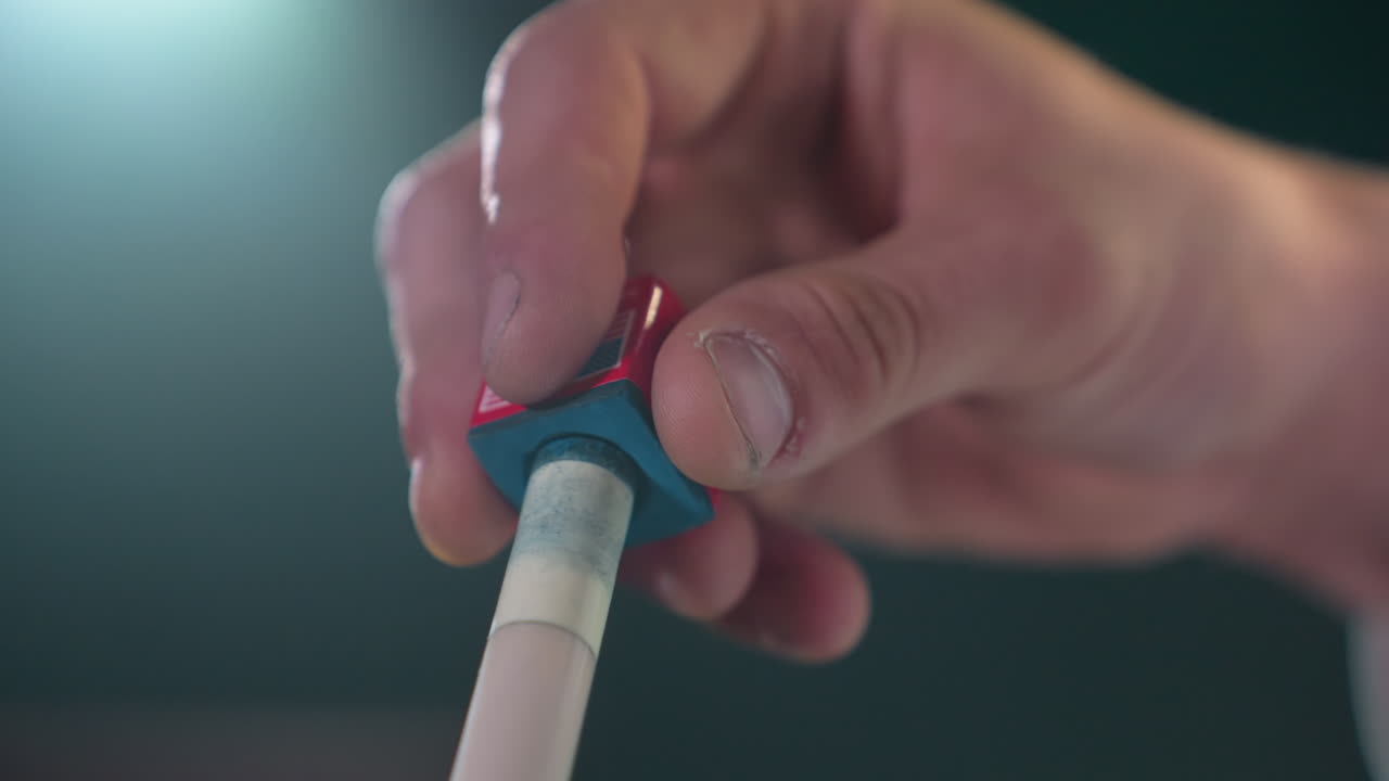 toma de primer plano de los dedos aplicando cuidadosamente tiza roja y azul al palo de señal antes del juego de billar. el agarre enfocado y el fondo borroso resaltan la precisión, la preparación y la atención