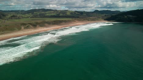 Filmischer-Drohnenflug-über-Surf-Break-Mit-Bergen-Im-Hintergrund