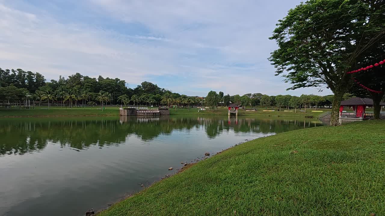 A tranquil lake in a tropical public park surrounded by lush greenery. Visitors enjoy recreation and relaxation in this serene setting.