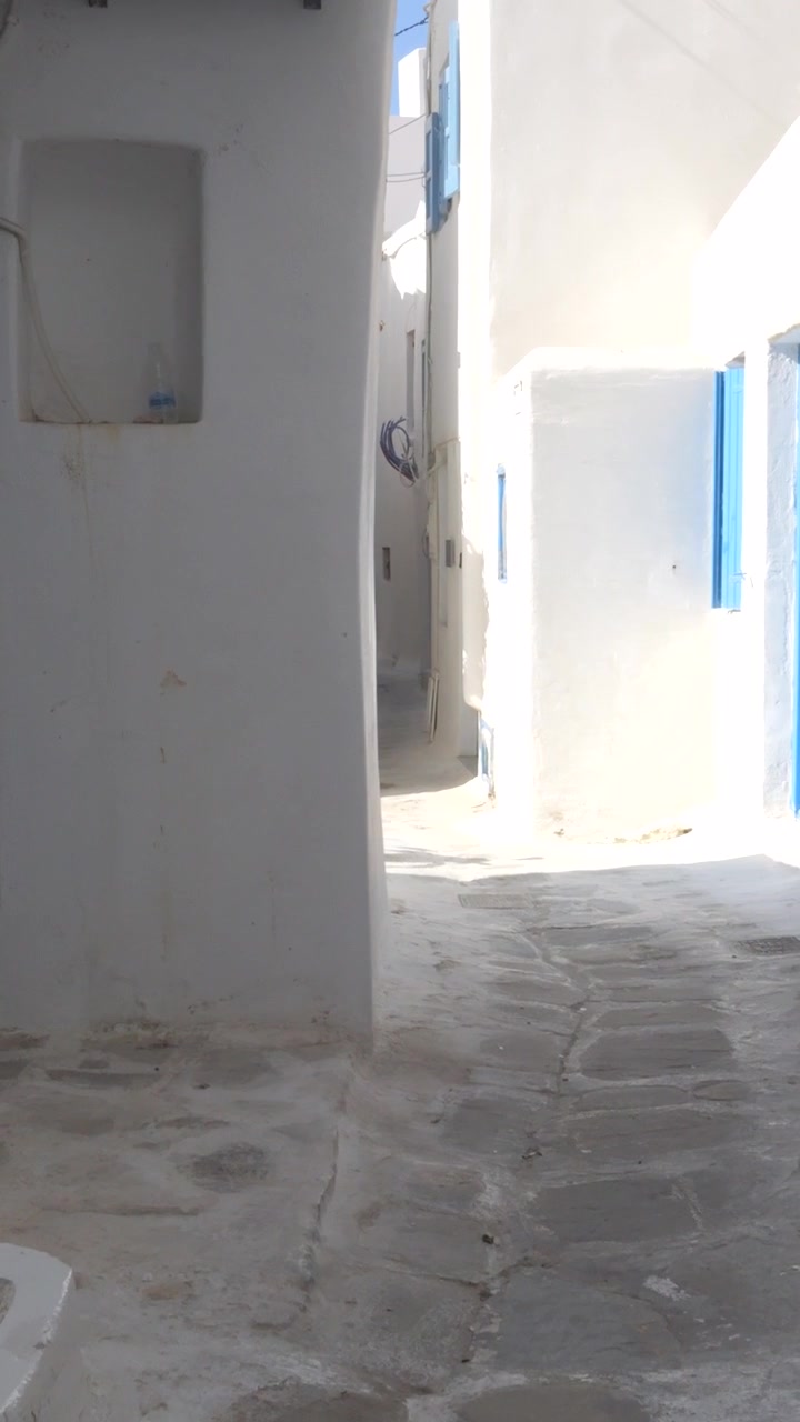 Ripresa POV verticale mentre si cammina per una tipica strada imbiancata a calce a Chora, Mykonos, che mostra la classica architettura cicladica.
