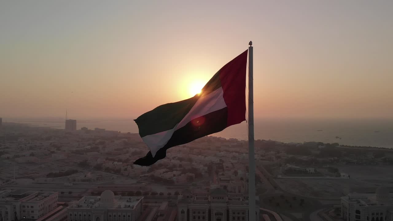 silueta, bandera de los emiratos árabes unidos ondeando en el viento, fondo de cielo y sol, el símbolo nacional de los emiratos árabes unidos sobre la isla de la bandera de sharjah, emiratos árabes unidos, video 4k