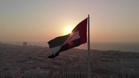 silhouette, flag of the united arab emirates waving in the wind, sky and sun background, the national symbol of uae over sharjah's flag island, united arab emirates, 4k video