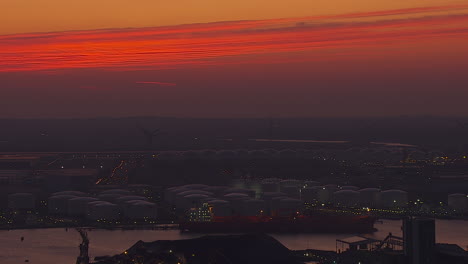 sun setting over antwerp industrial harbor and lights coming on over oil reservoirs