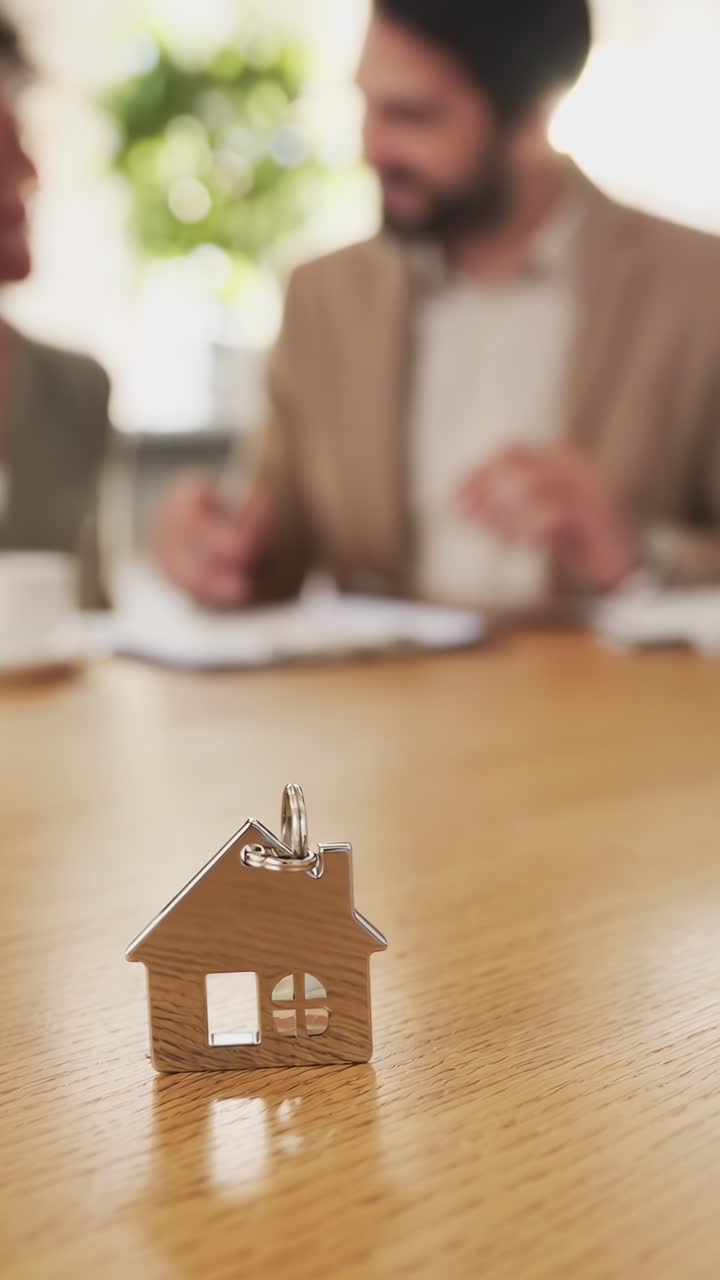 Primer plano de un llavero con forma de casa sobre una mesa, pareja borrosa al fondo, concepto de vídeo del hogar