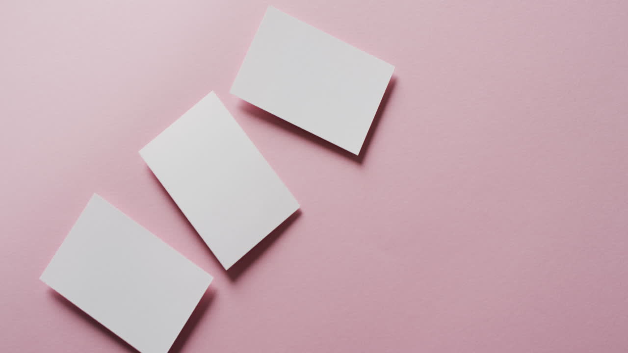 vista aérea de tres tarjetas de visita blancas dispuestas en fondo rosa, espacio de copia, cámara lenta