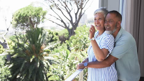 Ein-Gemischtrassiges-Paar-Genießt-Den-Sonnigen-Blick-Vom-Balkon,-Wobei-Die-Frau-In-Die-Ferne-Zeigt