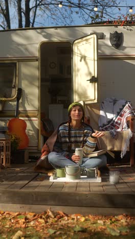 woman relaxing on a wooden deck by a camper van in autumn