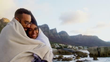 Couple-in-blanket-embracing-each-other-at-beach-4k