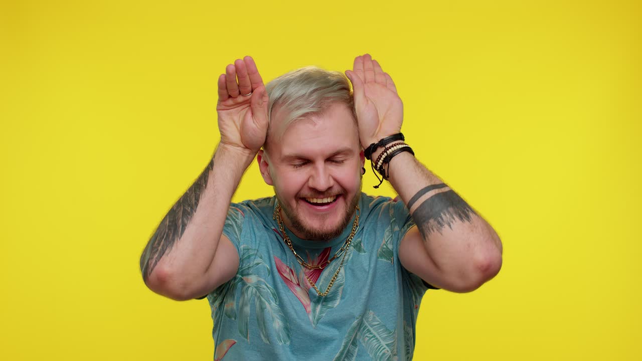 encantador hombre gracioso sonriendo amistoso, haciendo orejas de conejo gesto en la cabeza divirtiéndose engañando humor cómico