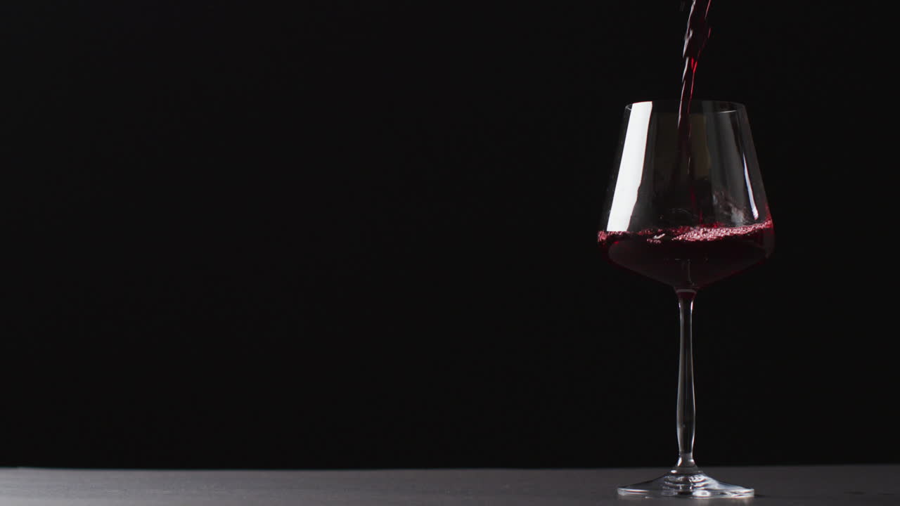 Vino rosso versato in un bicchiere su sfondo nero con spazio di copia.