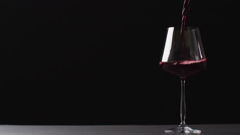red wine pouring into glass on black background with copy space