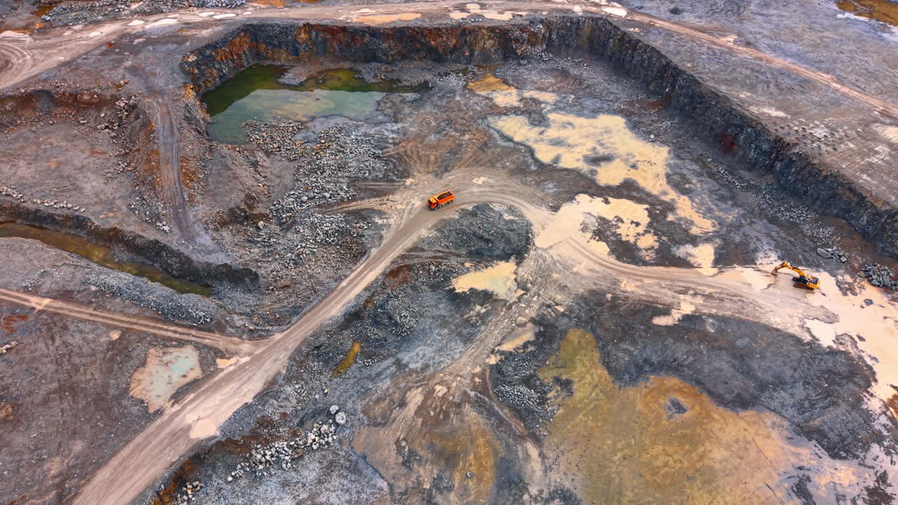 Mining site being built by water. Heavy machinery works on a mining site with a water body in the background during the day. Dust and gravel are visible
