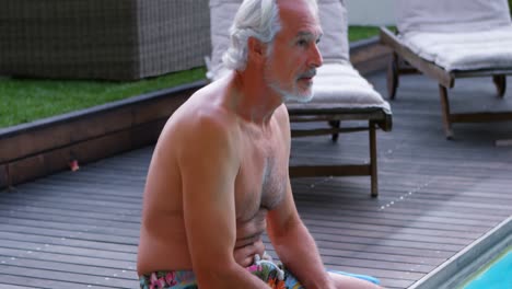 senior man sitting on the edge of swimming pool 4k