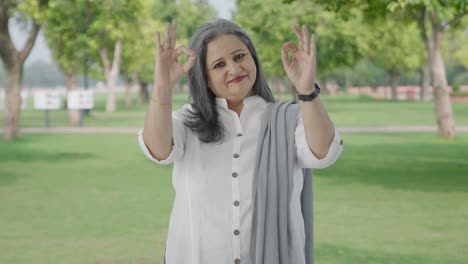 Happy-Indian-mother-showing-okay-sign-in-park