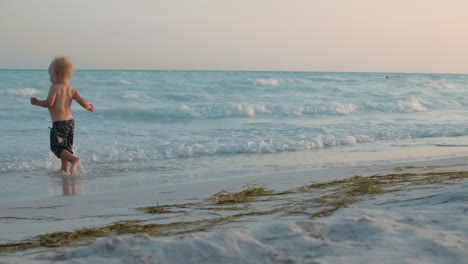 happy baby boy running at coastline. mom with child enjoying sea waves at beach.