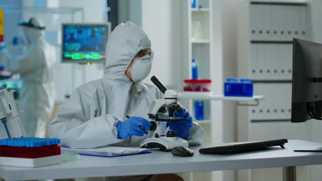 científico de investigación médica en traje de ppe llevando a cabo experimentos de adn bajo el microscopio