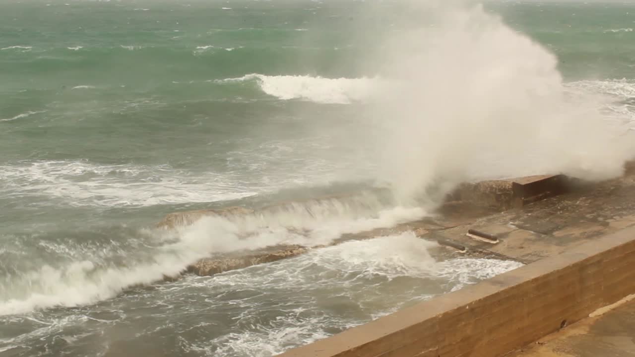 Big waves splashing on sea dock in Mellieha, Malta, on cloudy rainy day