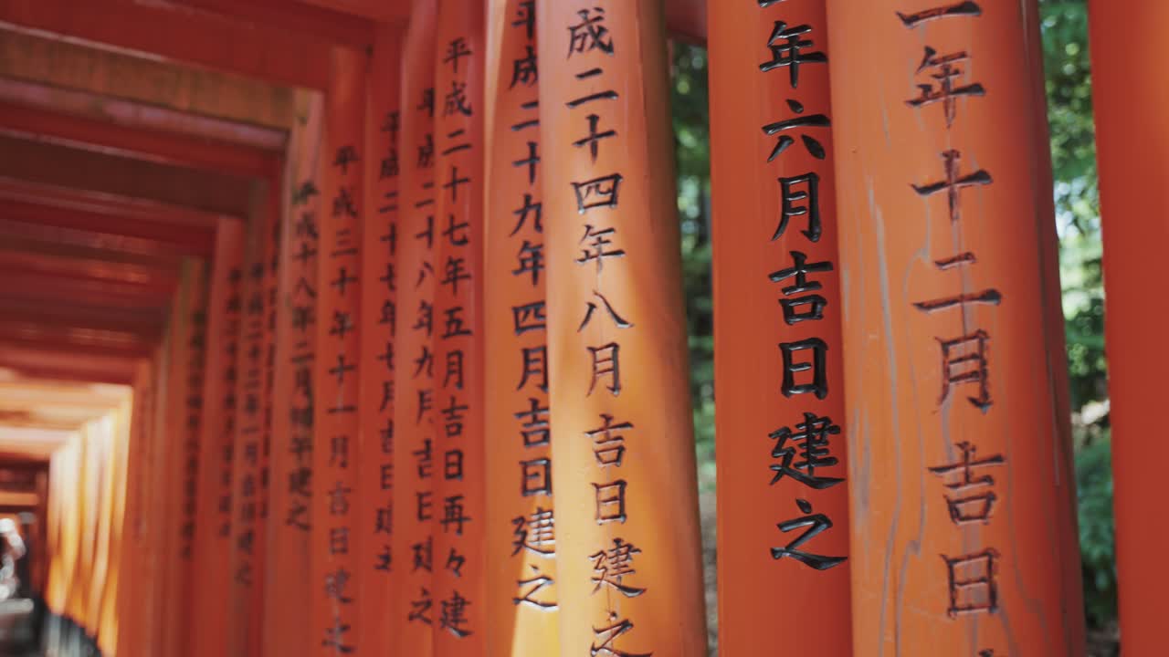 Video of vibrant orange torii gates of Fushimi Inari Shrine in Kyoto, adorned with elegant Japanese calligraphy, creating a mesmerizing spiritual passage rich in history and tradition.