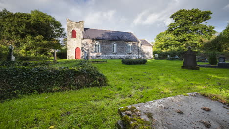 Time-lapse-of-rural-graveyard-with-church-in-background-in-Ireland-during-a-cloudy-day-with-rainbow-in-the-sky