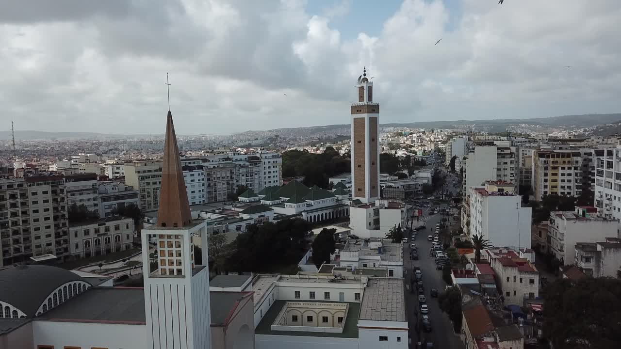 Ripresa cinematografica con drone che mostra una chiesa e una moschea che sorgono insieme a Tangeri, Marocco, come un potente simbolo di armonia interreligiosa e coesistenza pacifica