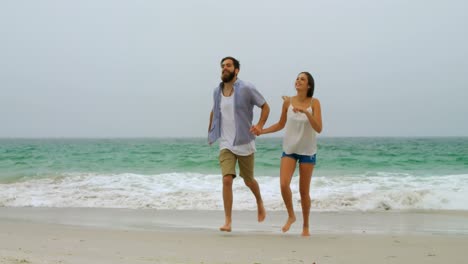 vista frontal de una pareja caucásica corriendo de la mano en la playa 4k