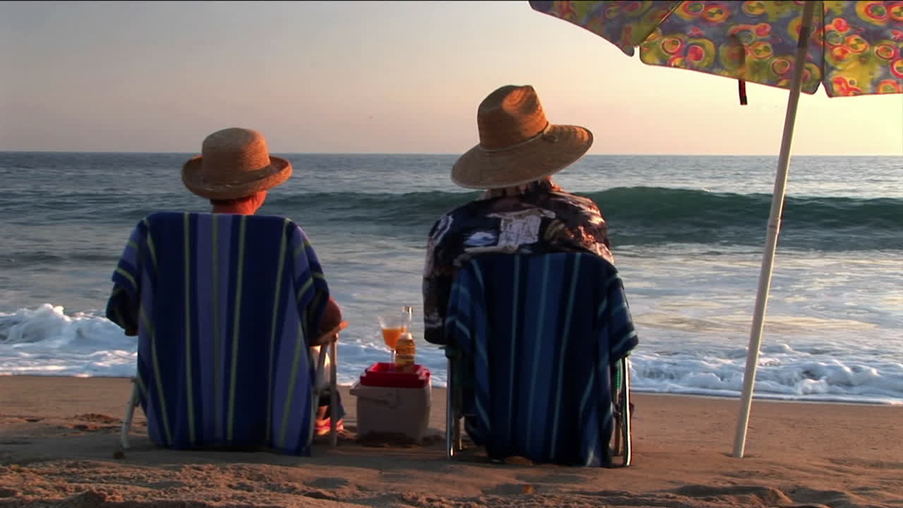 una pareja de ancianos comparte bebidas bajo una sombrilla en la playa