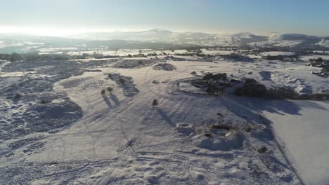 Snow-covered-rural-winter-countryside-track-footprint-shadows-terrain-aerial-view-descending