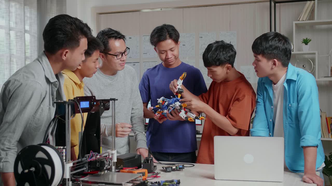 노트북과 3d 프린팅을 가진 아시아인 남자가 학교에서 소년들에게 사이보그 손을 조립하는 법을 가르니다.