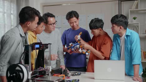 asian man with a laptop and 3d printing teaching the boys assembling a cyborg hand at school