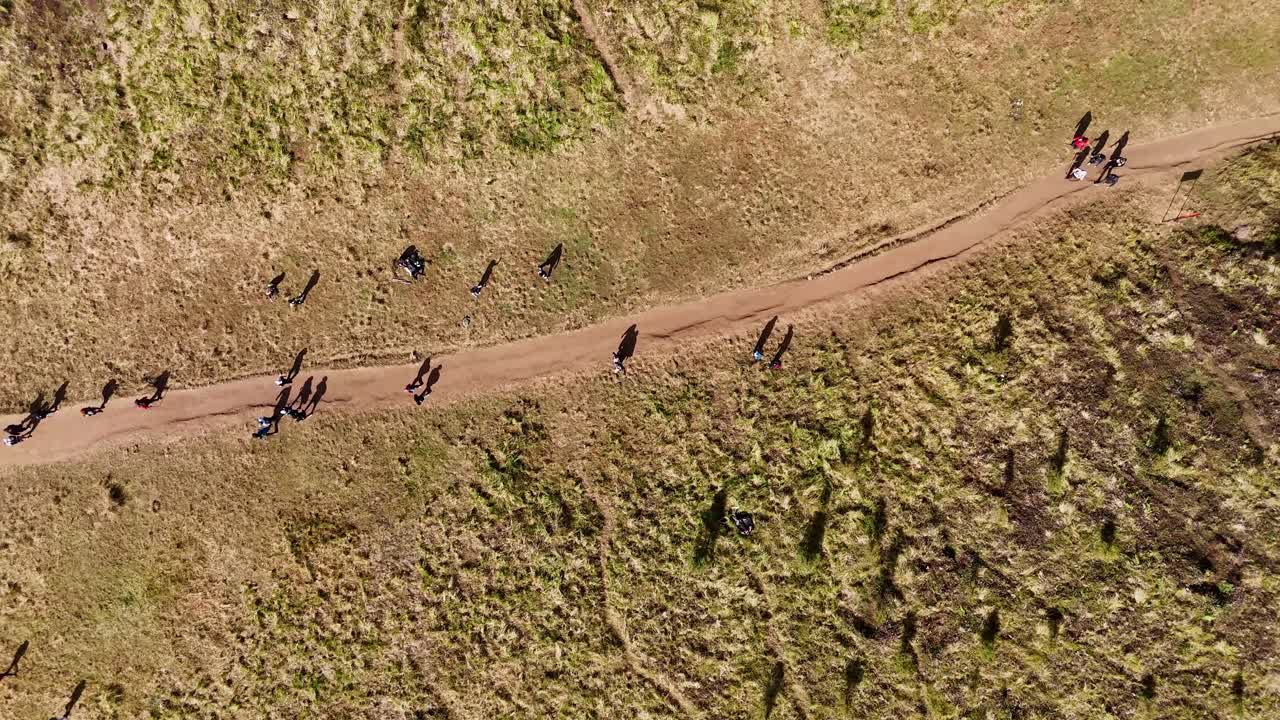 Aerial top-down view of hikers walking along a trail through dry grasslands. Mount Prau, Indonesia