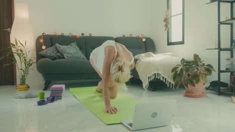 woman practicing yoga at home via laptop