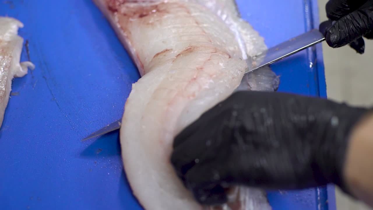manos de chef con guantes negros pelando filete de pescado con un cuchillo afilado en una tabla de corte azul