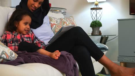 young mother using a digital tablet with her daughter on the sofa at home 4k