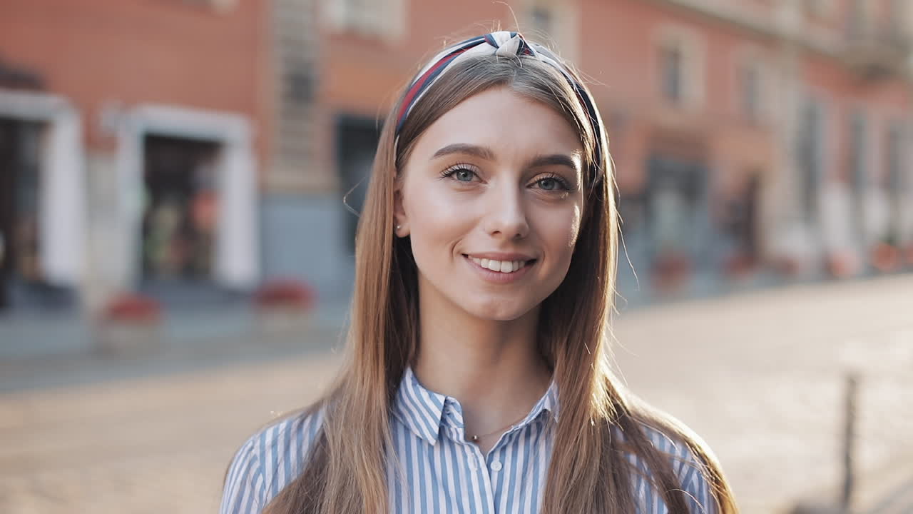 Giovane donna sorridente che guarda in camera su una strada cittadina.