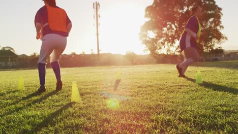 Diverse-group-of-female-baseball-players-exercising-on-pitch,-running-between-cones