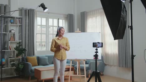 asian female teacher with marker pen shoots video by smartphone camera while teaching math at home