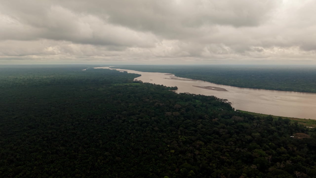 Majestætisk luftfoto af den mudrede Amazonflod, der strømmer gennem den tætte grønne regnskov under en overskyet himmel.