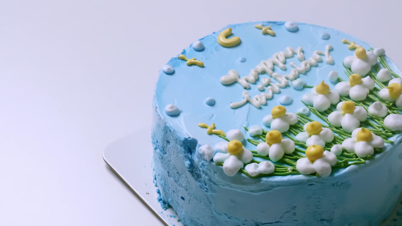 primer plano de la parte superior de un pastel de cumpleaños con glaseado azul y decorado con flores blancas y amarillas, con felicitaciones de cumpleaños en la parte superior