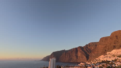 sunset timelapse of los gigantes cliffs in tenerife on a clear day with the city lights illuminating